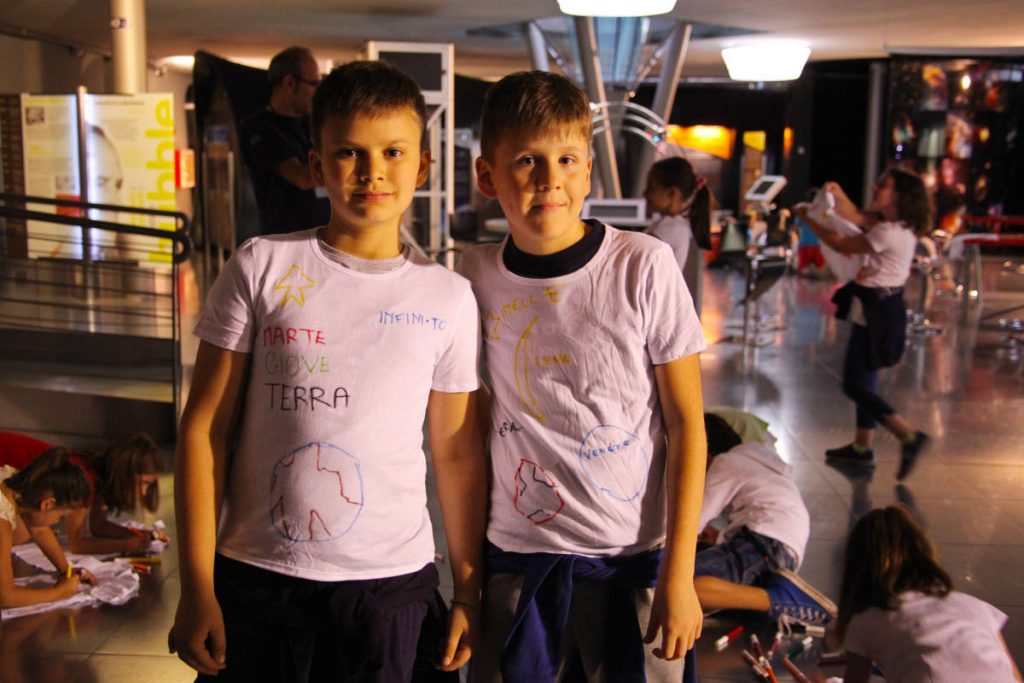 Bambini di circa 10 anni che decorano delle t-shirts con stelle e pianeti durante un laboratorio