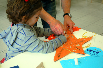 Bambina di circa 4 anni che decora assieme ad un adulto una stella di cartone